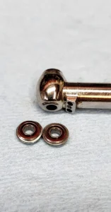 Dental handpiece head on a repair bench beside two replacement turbine bearings with copper-colored sealed faces